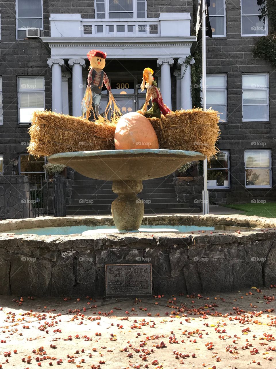 A pair of decorative scarecrows perched on hay bales with a pumpkin in the fountain at the old Crook County Courthouse in Prineville in Central Oregon on a beautiful fall day.