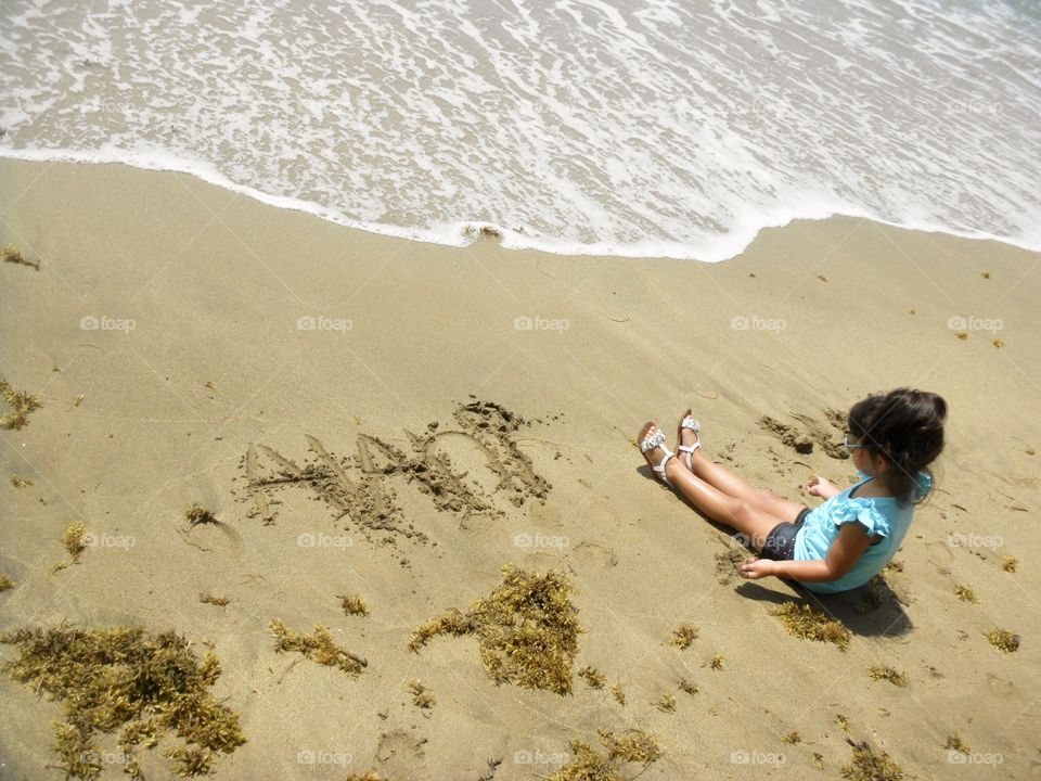 Girl writing on sand and playing at the beach 