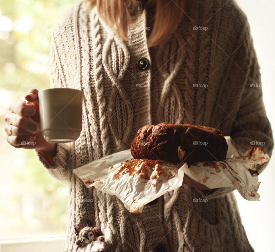 Girl in a knitted boho sweater holds in her hands a white mug with coffee and a homemade banana cake