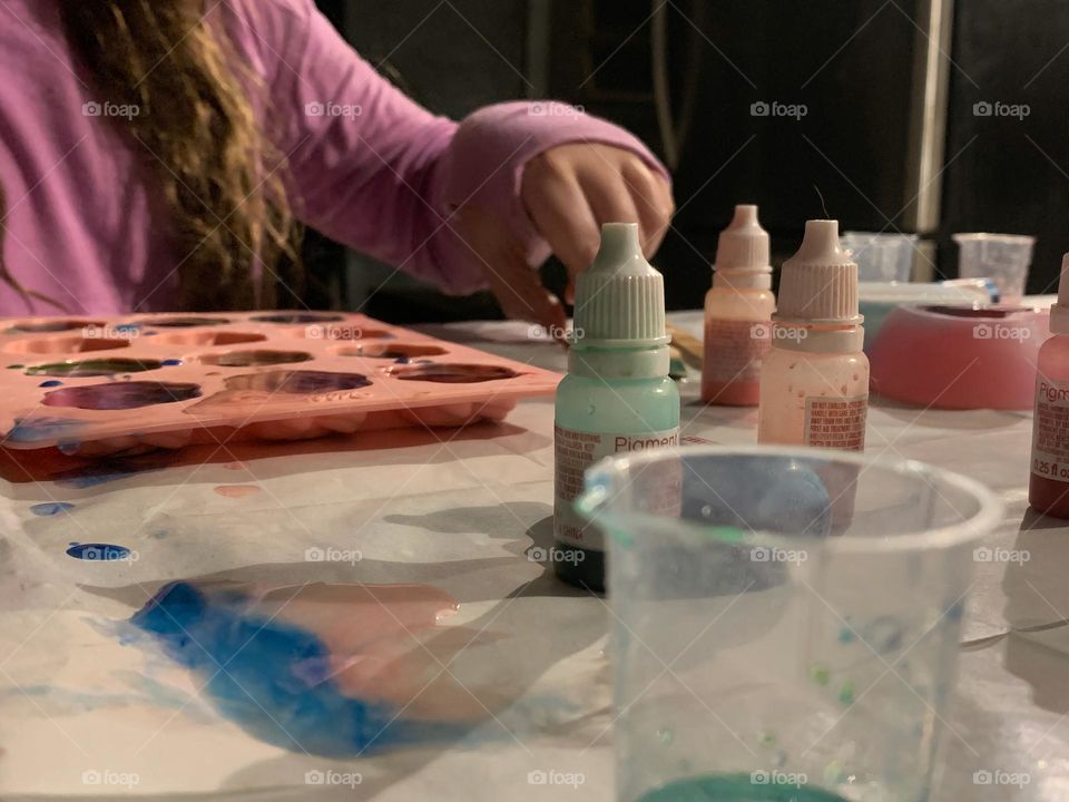 Child girl making a craft project with colorant and epoxy in roses molds and making two small bowls.