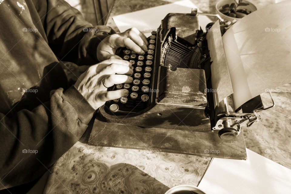 Male writer typing his book on an old rare typewriter at the table