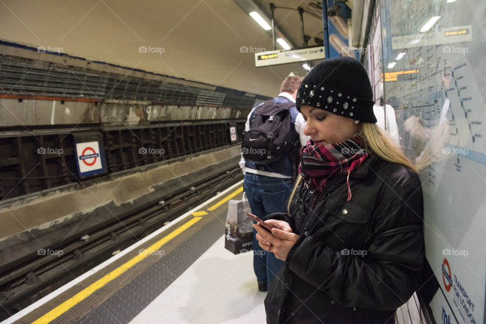 Woman standing in the subway in London and looks at her cell phone.