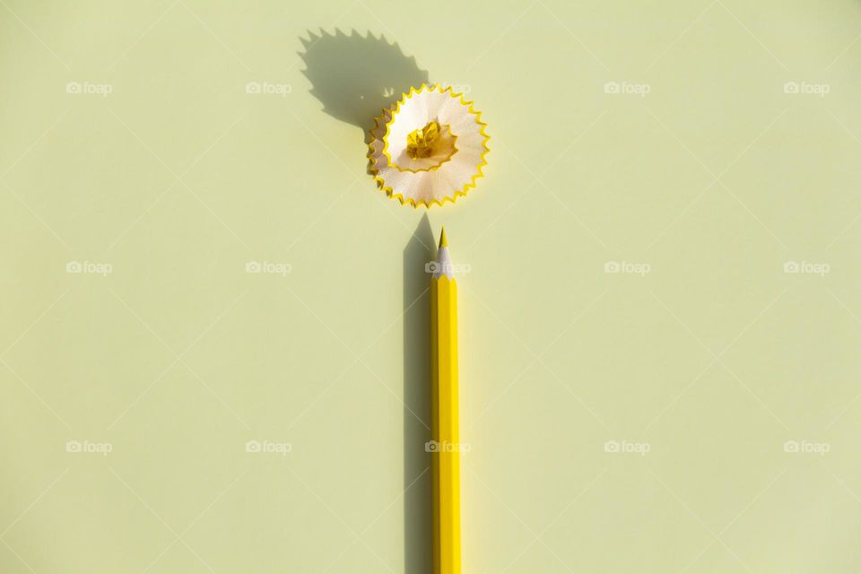 The yellow, colored pencil for drawing in the album is sharpened and lies on a yellow background with a pronounced shadow on a sunny day from bright, sunlight.
