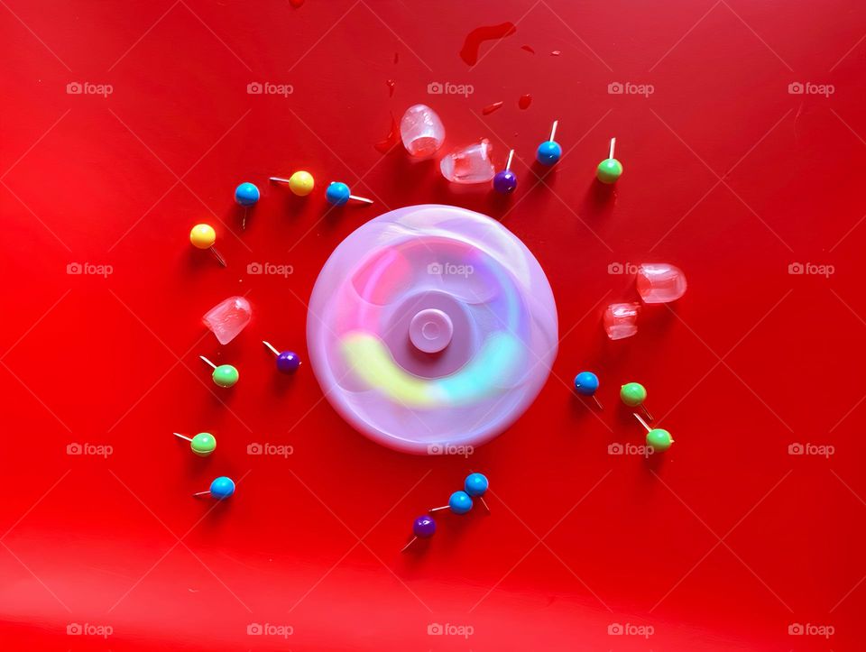 Multicolor Fidget Spinner Time In Motion Long Exposure With Smiley Face Seems To create Cold Ice Cubes On A Red Background.