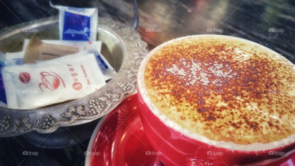 Cappuccino coffee with a selection of sugars in the background. Cappuccino is an Italian coffee beverage that is traditionally prepared with double espresso, and steamed milk foam.