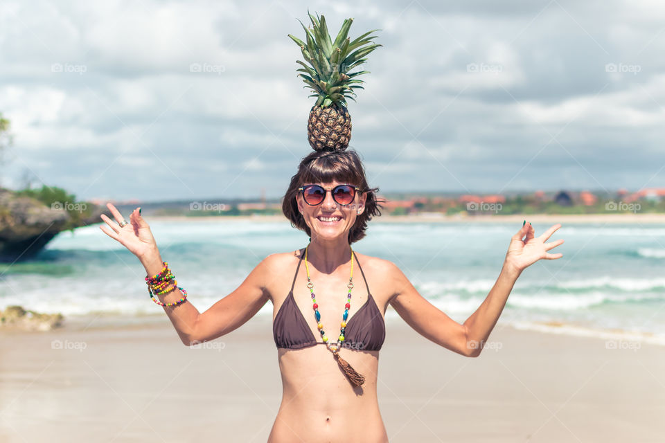 The girl smiles and holds a pineapple on her head.