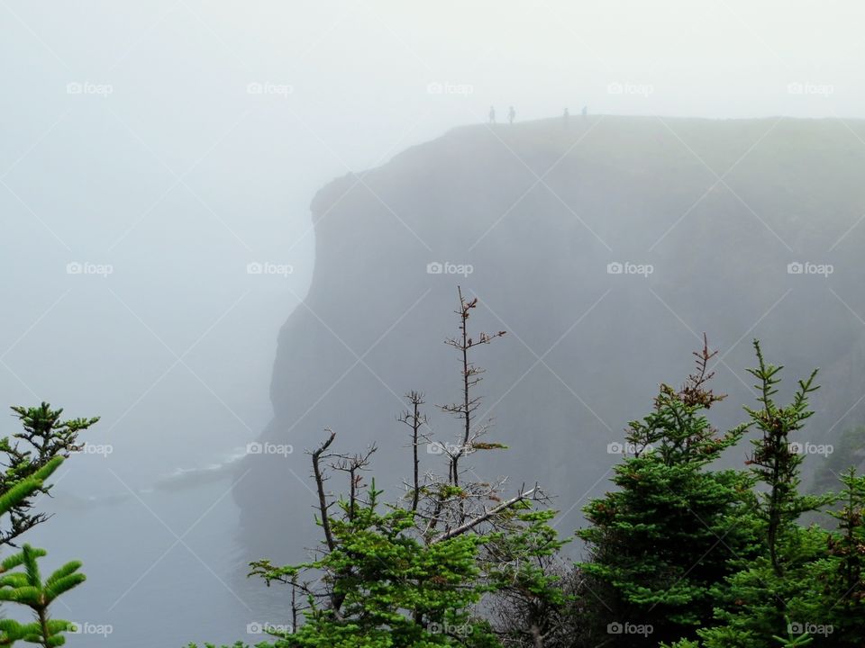 Hikers and a couple soon to be engaged hiking along the steep and foggy cliffs of the Skerwink Trail along the rugged and beautiful coast of Newfoundland and Labrador 