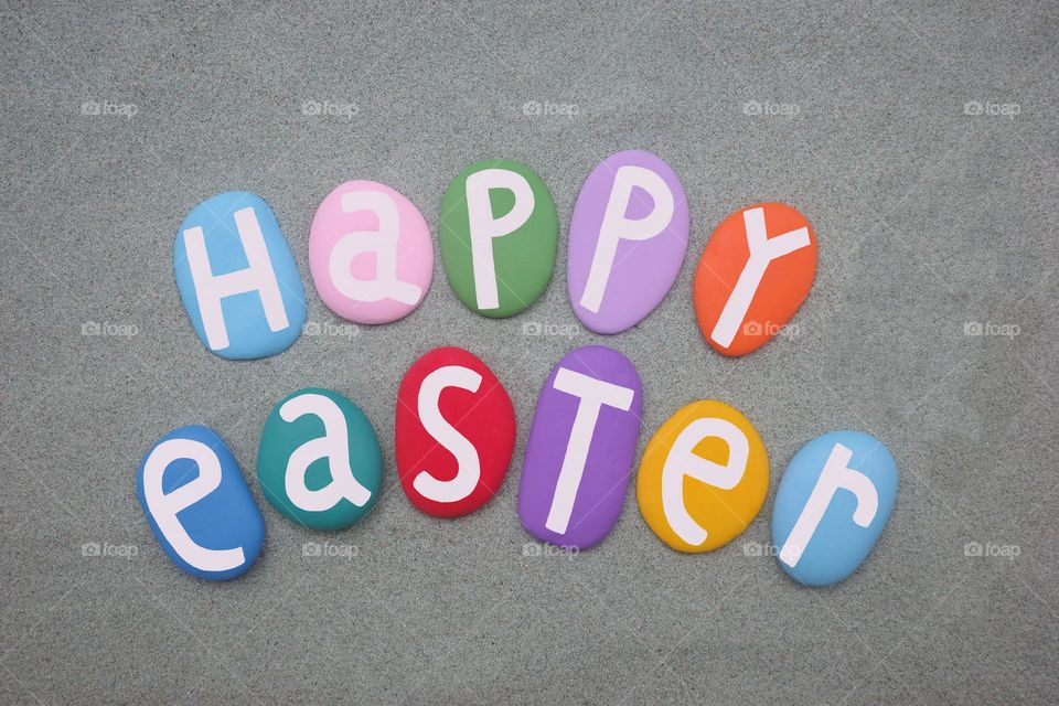 Happy Easter message composed with hand painted stone letters over green sand 