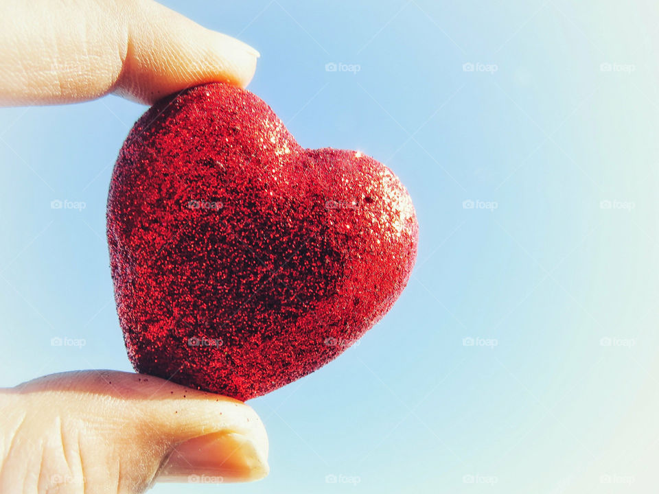 Hand Holding Shiny Red Heart Against The Sky