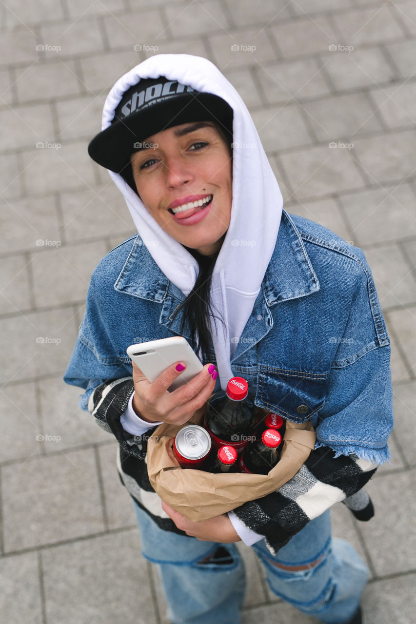 cute girl, blogger, walks on the street, holds in hand.  phone, taking pictures, drinking Coca-Cola.  the girl is stylishly dressed