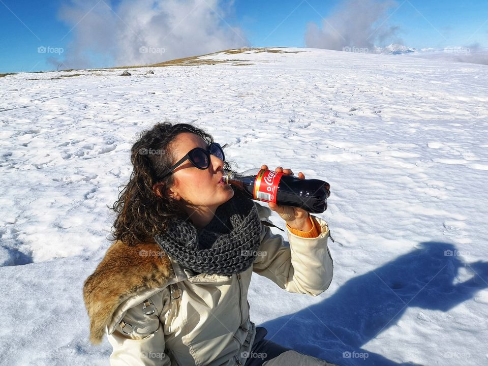 girl drinks Coca Cola sitting on the snow in the mountains