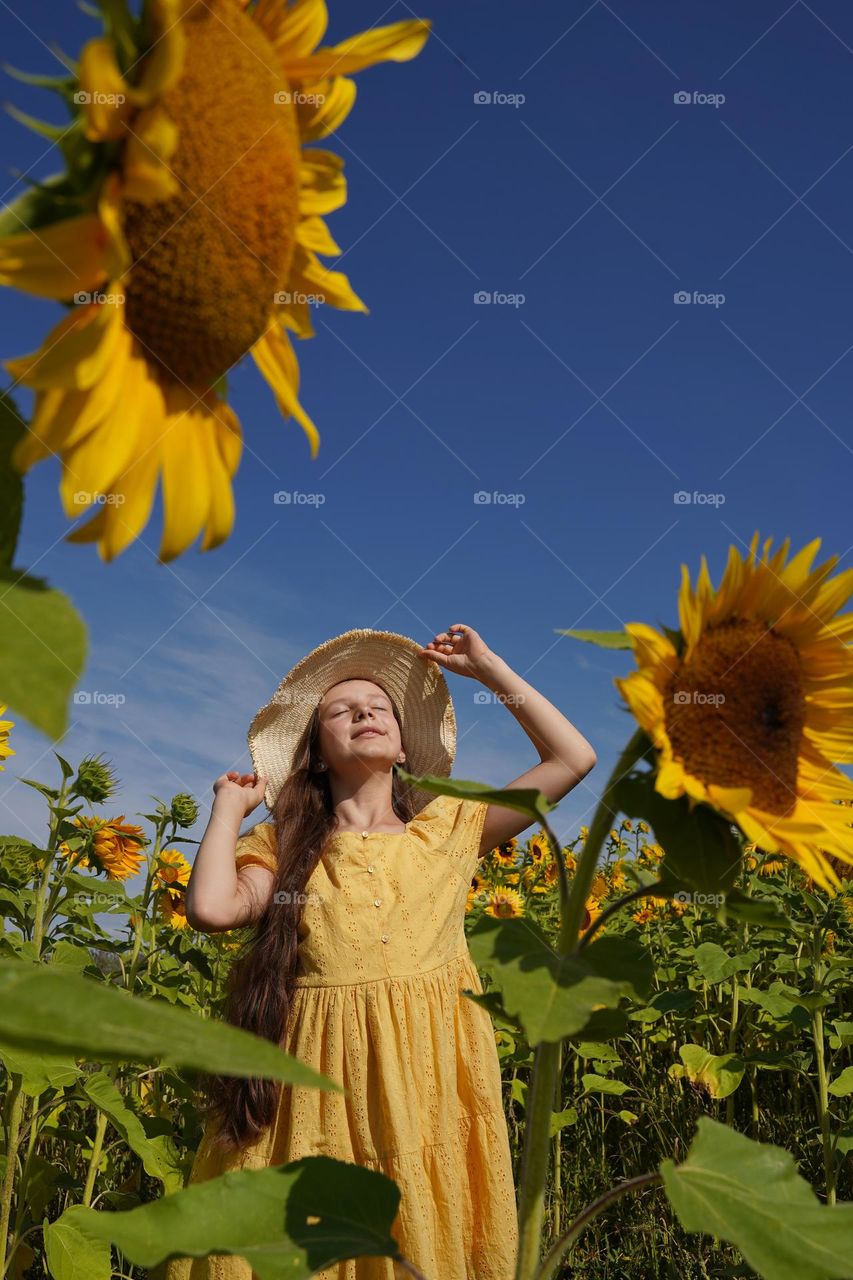 Girl in a hat on a sunflower field on a sunny summer day