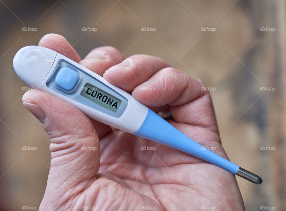 Male hand holds clinical thermometer with covid-19 text on the screen during global covid-19 or corona pandemic.