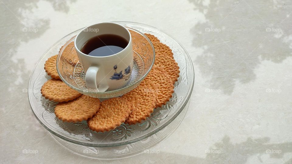 Coffee with biscuits, coffe in a white ceramic glass and biscuits in a transparent glass plate