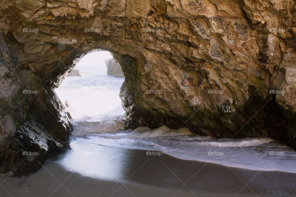 Gentle waves crashing through a small sea cave at low tide at Sharktooth Beach in Davenport, California on a clear, bright sunny day