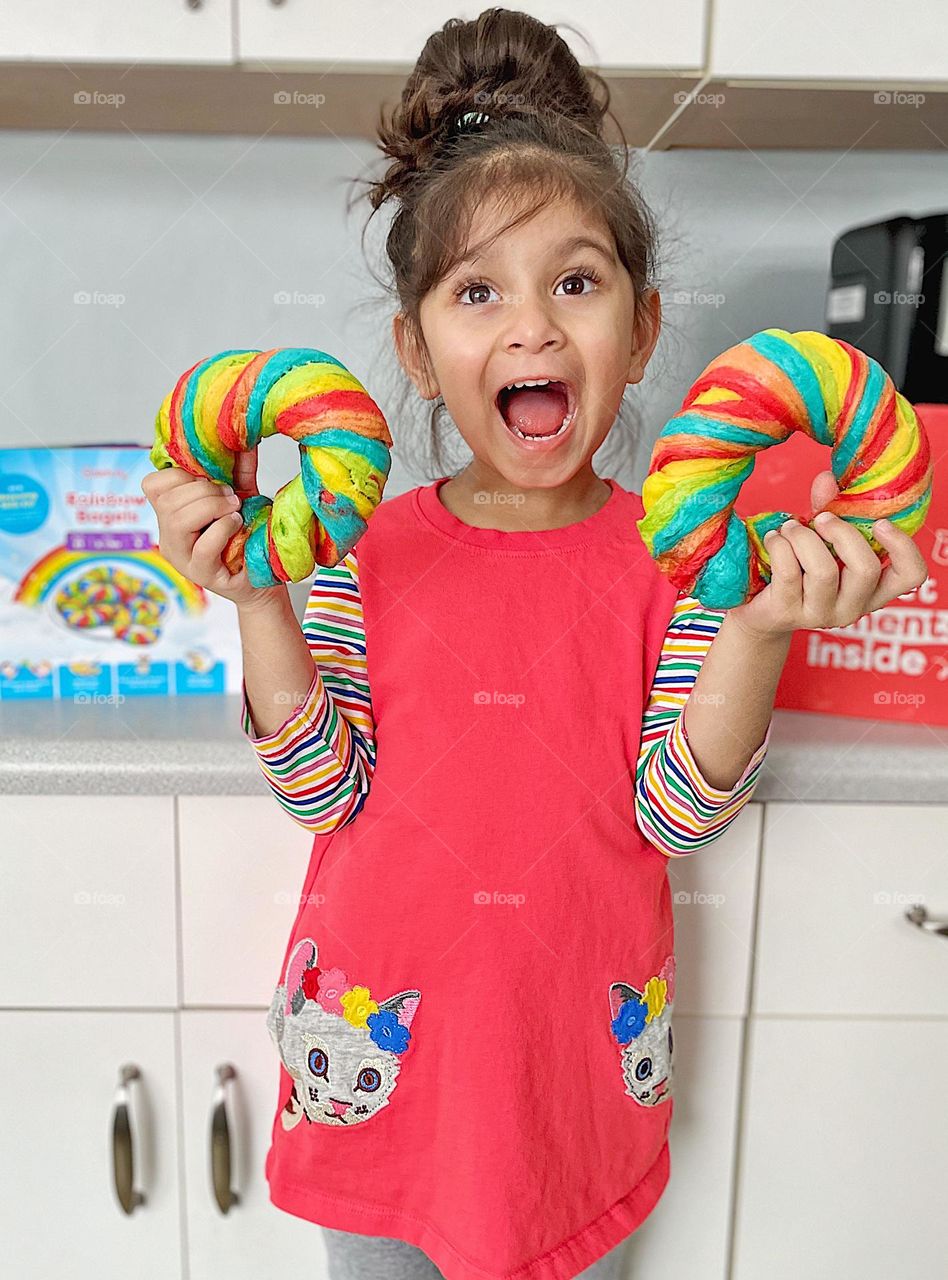 Child holds two rainbow bagels, making brightly colored bagels, delicious and colorful food, baking with mommy, in the kitchen baking with Mommy