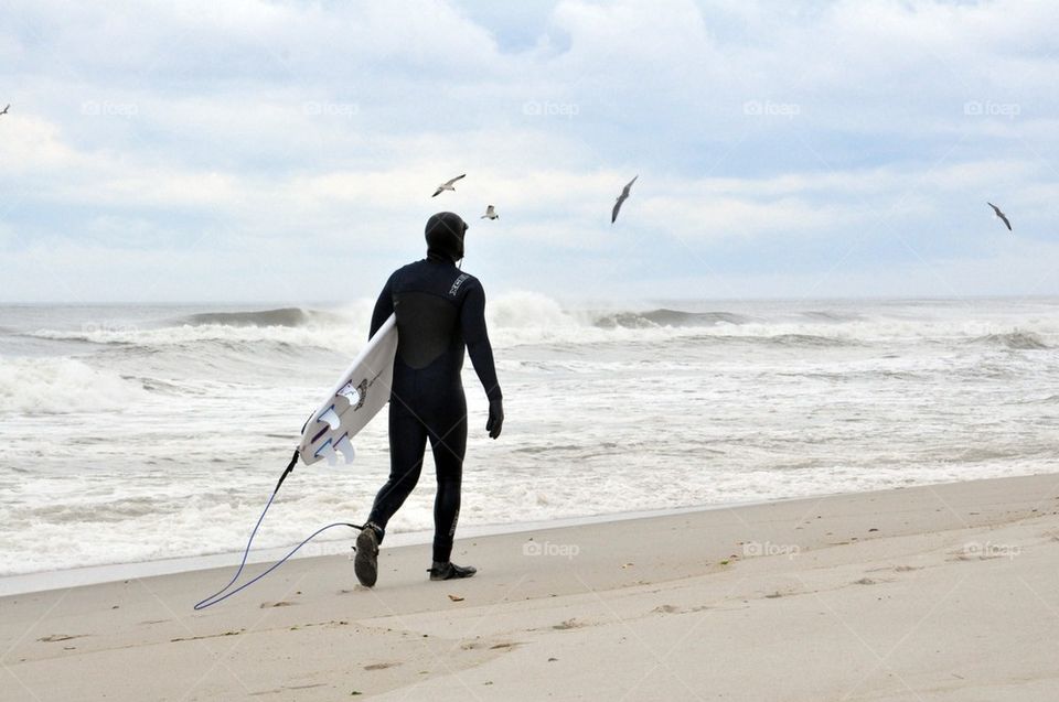 Surfer seen with board and wetsuit walking by the ocean 