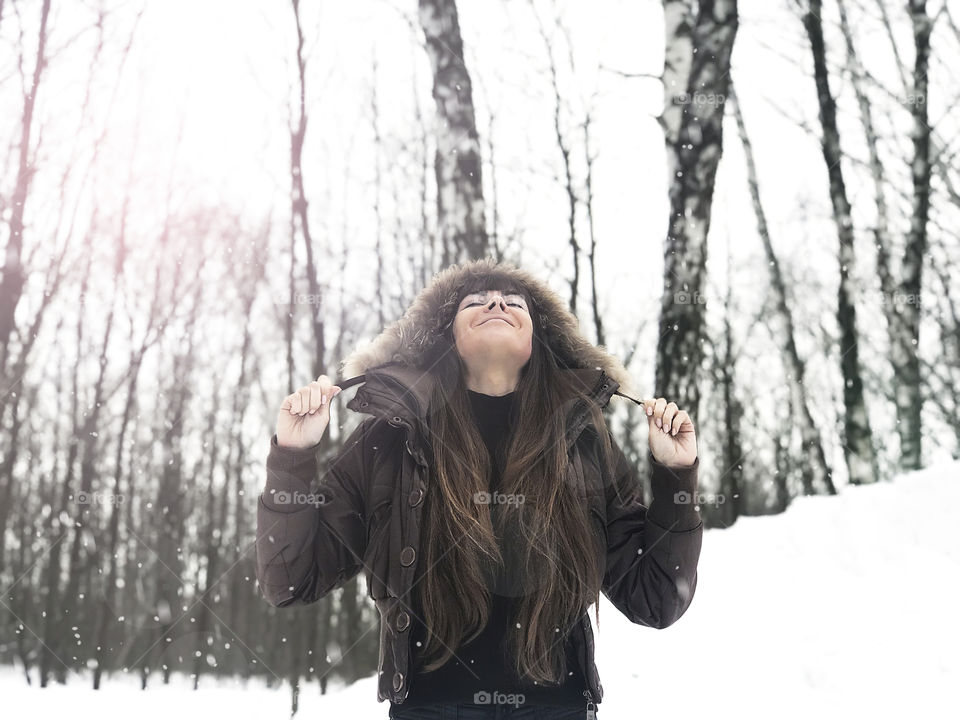 Young woman with long hair enjoying fluffy snow in winter forest 