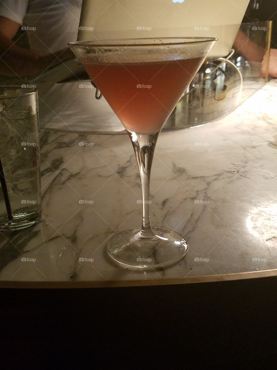 A vodka alcoholic drink in a classic V-shaped glass at a bar in some dark lighting.
