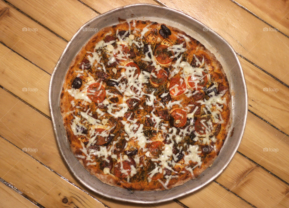 Pizza in the round metal tray on wooden background