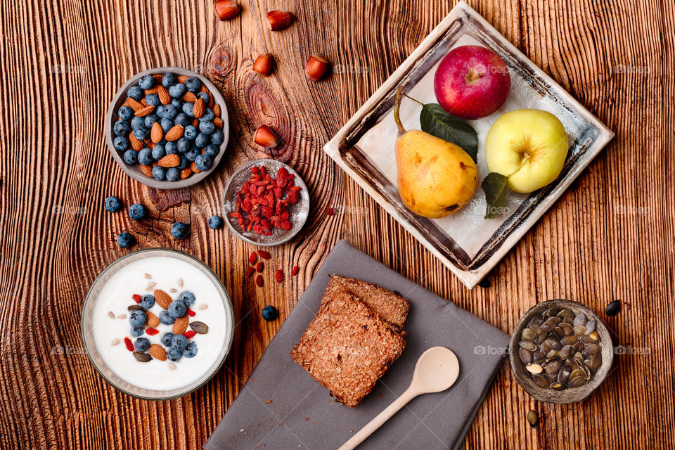 Breakfast on table. Yogurt with added blueberries and roasted almonds. Muesli cookie, apples and pears on wooden table. Light and healthy meal. Good quality balanced diet. Flat top-down composition