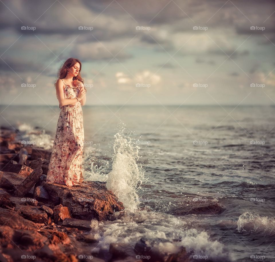 Beautiful young woman near sea at sunset