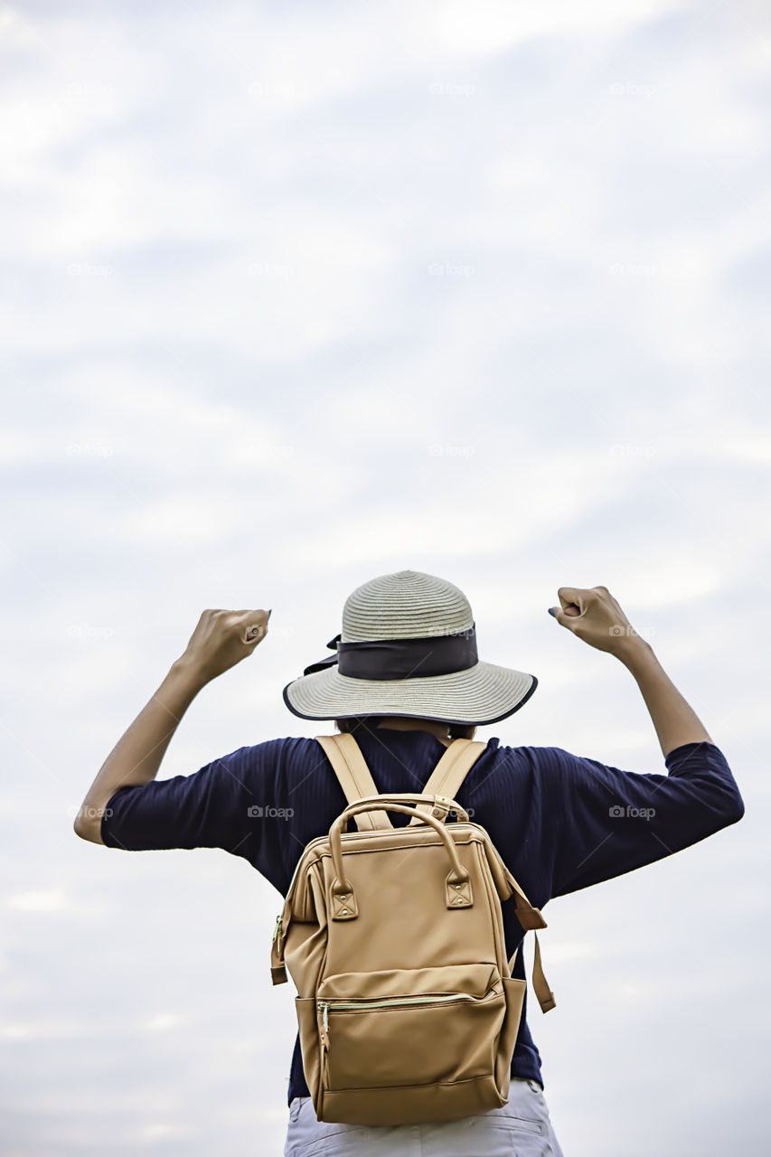 Women shoulder backpack and  raise their arms up to the sky.