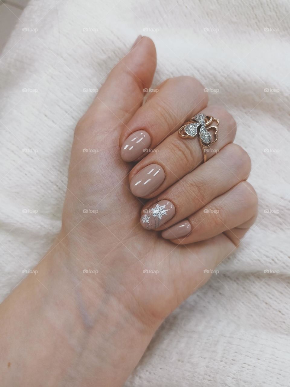 manicure on a female hand, the color of nails is coffee with milk, a white snowflake, female hands on a white background, a warm fluffy scarf, nail polish, a gold ring on a finger, a female hand with a ring