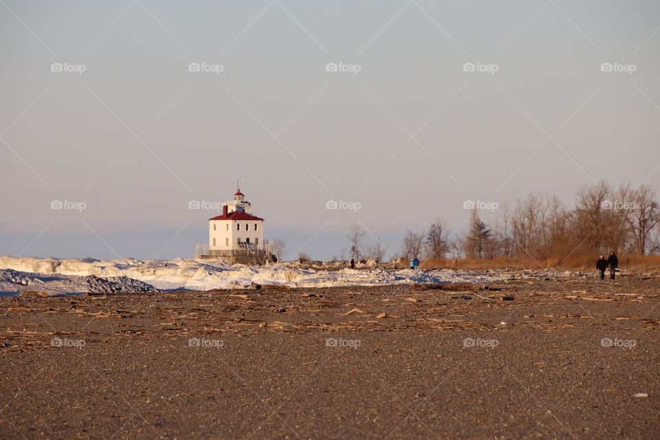 People walking on beach in Winter with lighthouse in background 