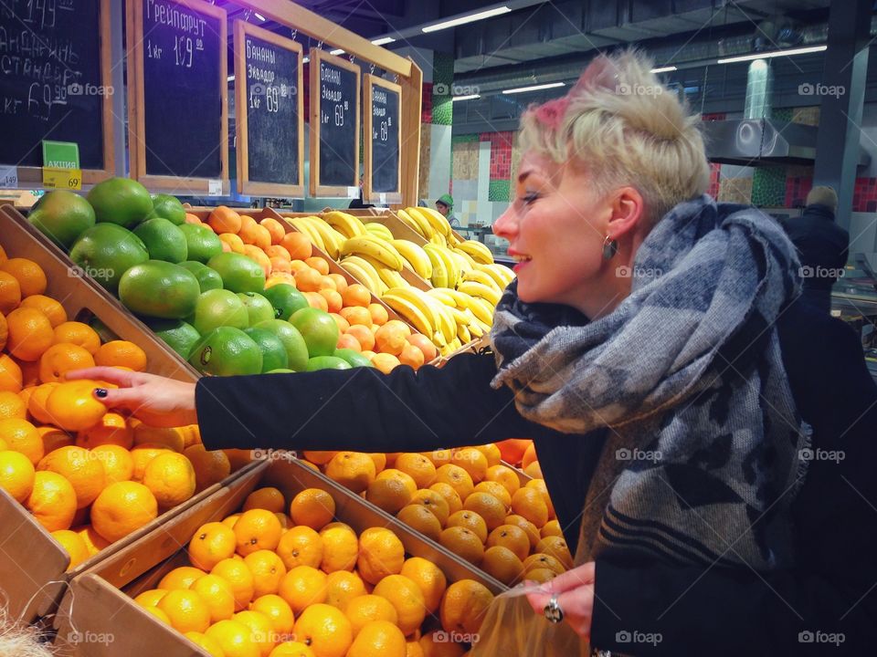 Young wooman with white-pink hairs choosing mandarins from the row of fruits in the marketplace