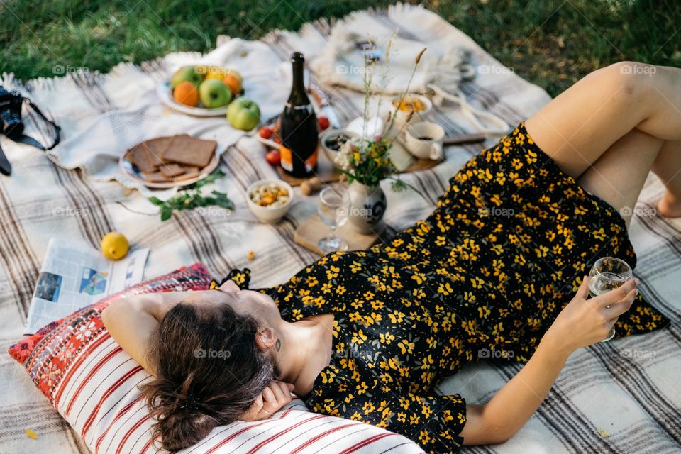 Woman enjoying a glass of wine while sitting in the garden having a picnic with fresh fruits, vegetables, cheese and bread in summer time.