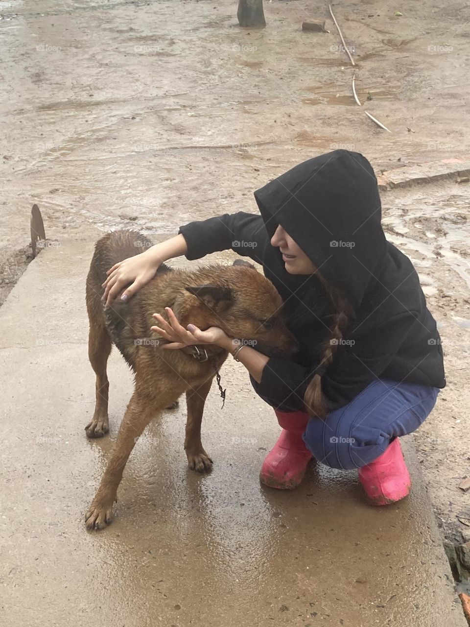 Cachorro e menina molhados na chuva, atrás barro e água.