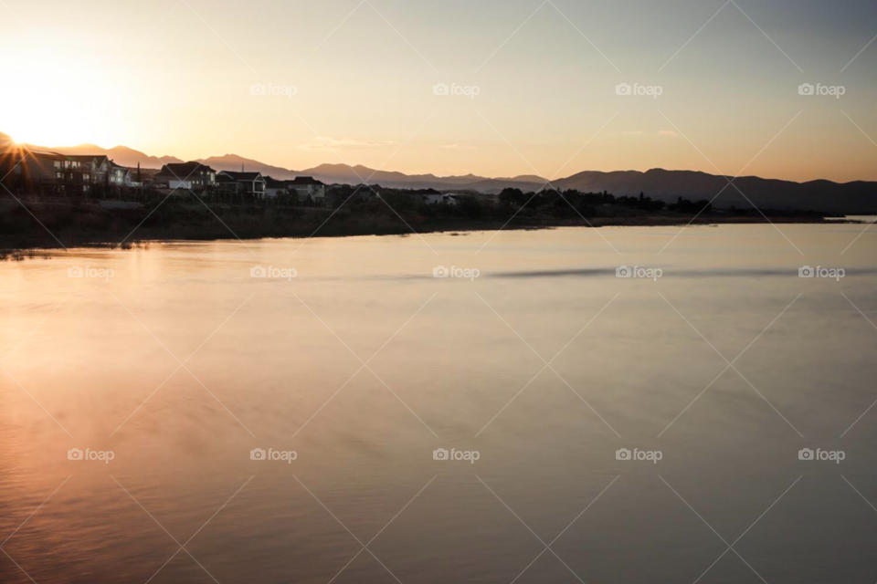 Sunset photo of a housing development with smooth, reflective water and mountains in the background.