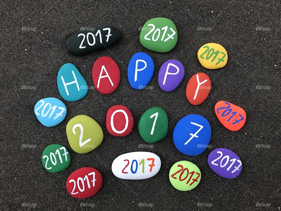 Happy 2017 message with multicolored stones over volcanic black sand 