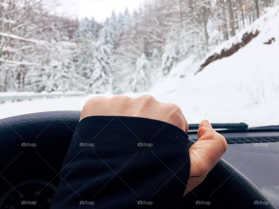 Hand on the steering wheel with snowy scenery seem through the windshield 