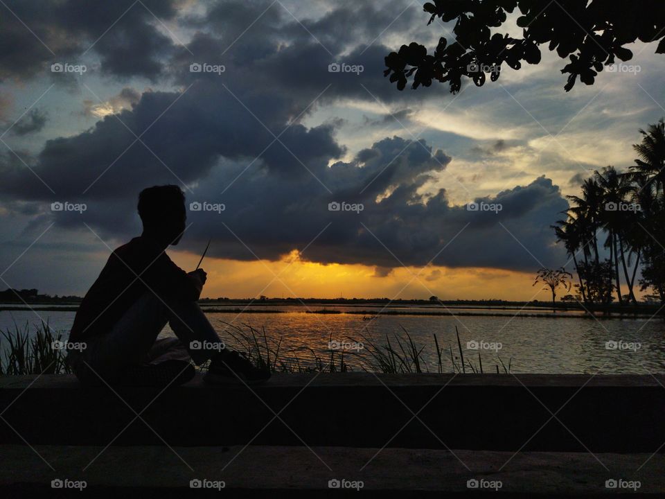 the sunset with orange colored clouds. and there is a human being who is posing with a sunset background