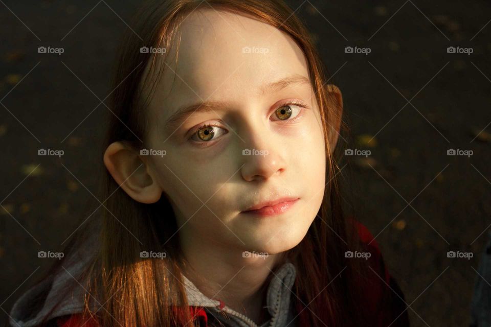 Cute little girl looks at the camera while the sun is reflected in her eyes