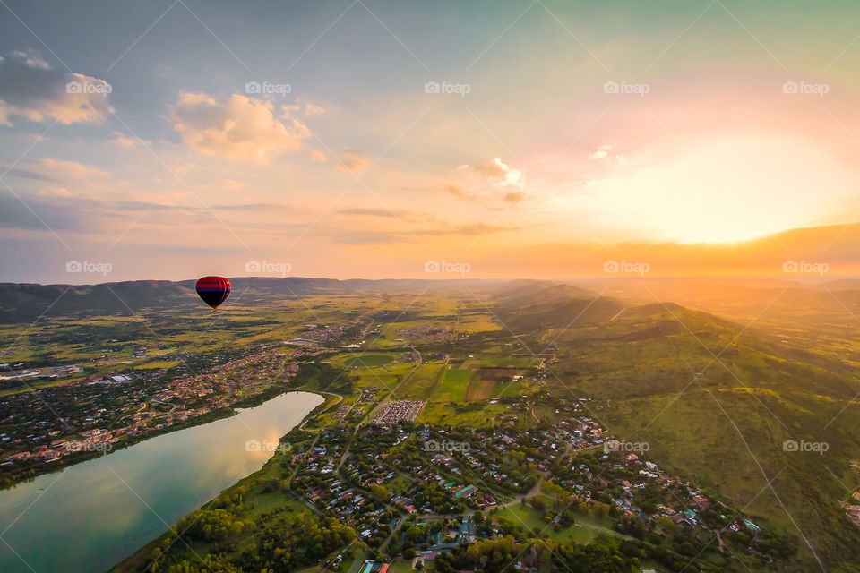 Hot air balloon sunrise over valley with lake and river and town in distance. Golden vibrant colors. Scenic balloon trip in Africa.