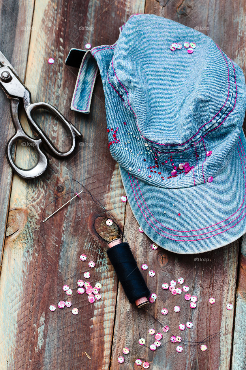 Decorating cap with sequins using thread needle and scissors following diy ideas on wooden table