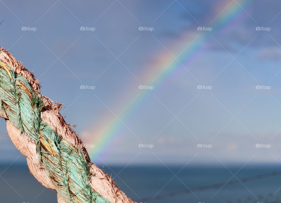 Rainbow over the sea with nautical marine rope foreground sporting similar pattern and colours 