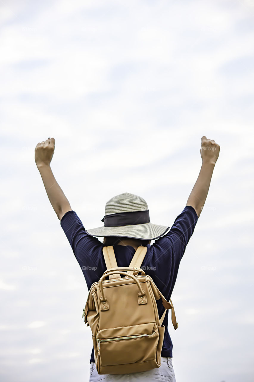 Women shoulder backpack and  raise their arms up to the sky.