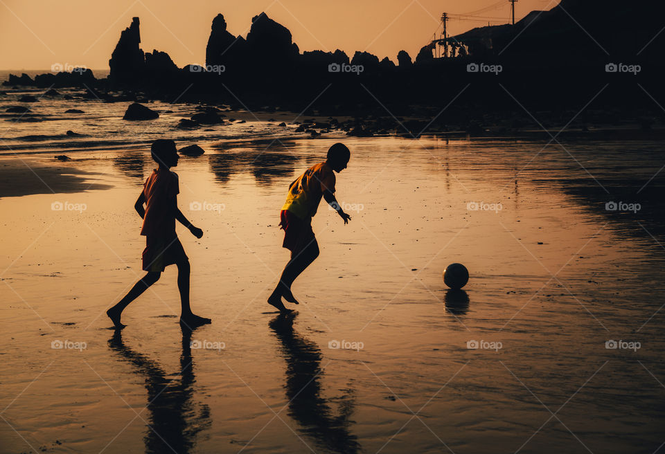 Two boys play soccer on beach in dusk, Goa, India
