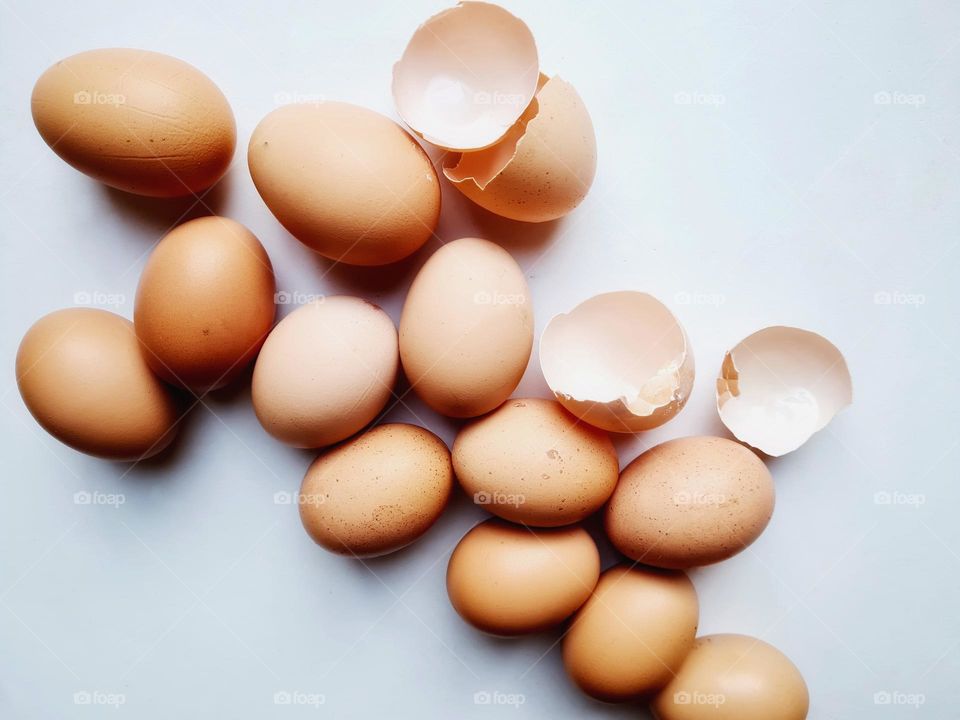 broken eggs and eggshells resting on white background