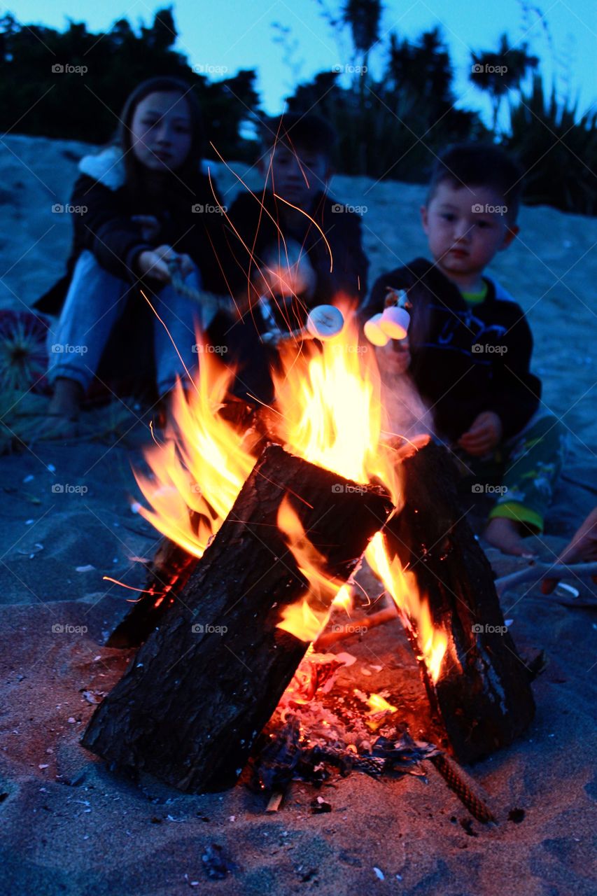 Child sitting on sand in front of campfire