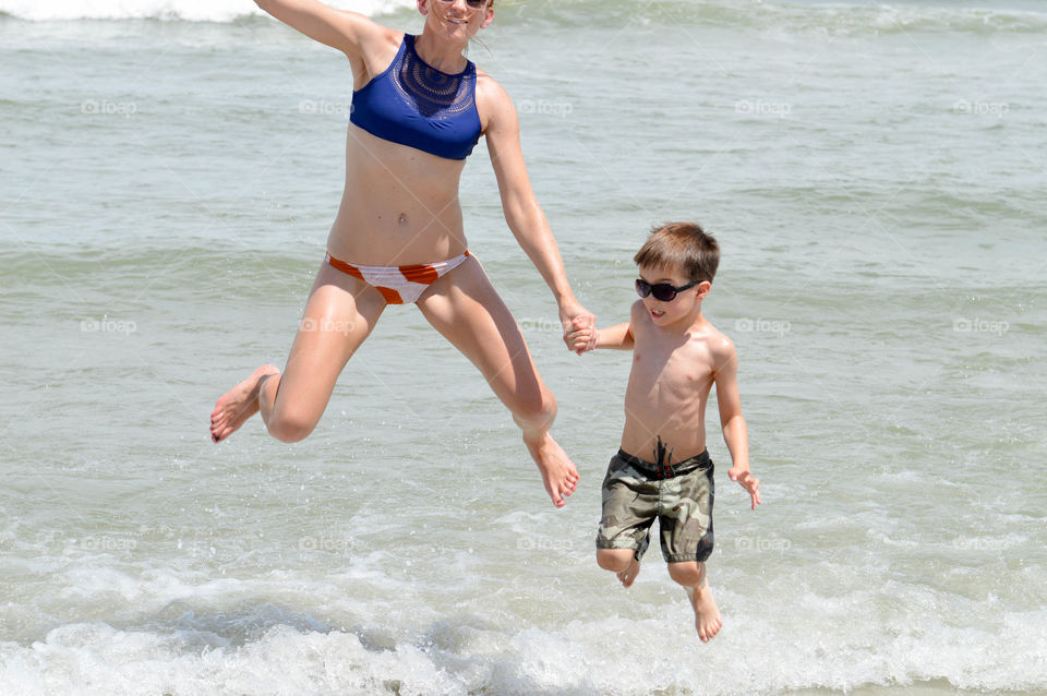 Woman and boy smiling and jumping in the waves of the ocean