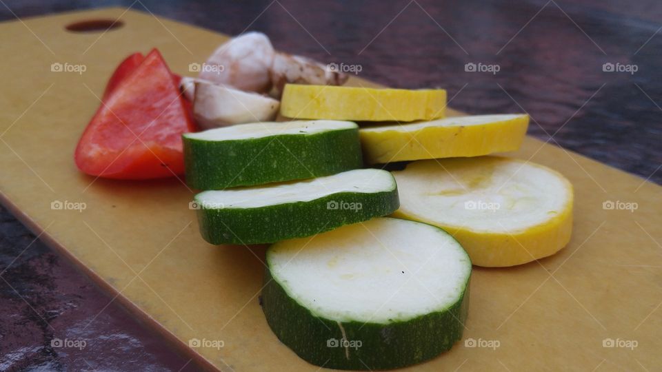 fresh cut vegetables on cutting board yellow squash cucumbers red bell peppers and mushrooms