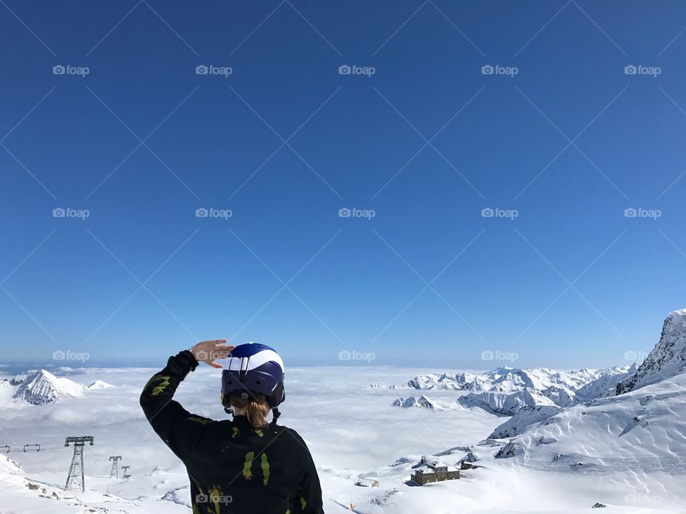 A back view of a person looking at the mointains covered in snow, against blue sky