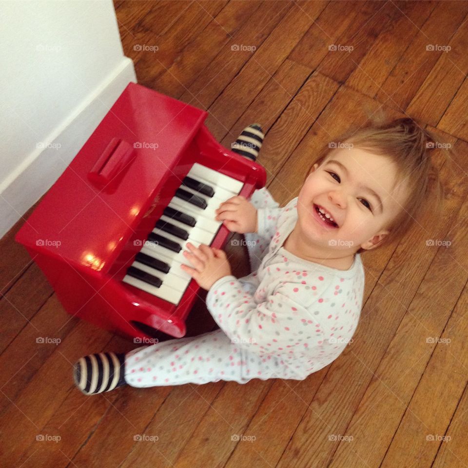Happy baby in pyjamas playing red piano