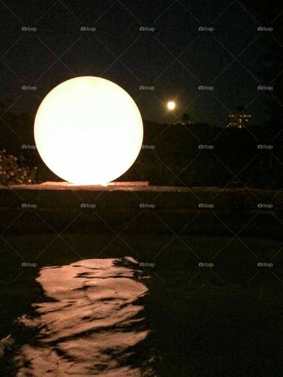 A big round shapped light reflecting in the water of a hot tub with the full moon in the background