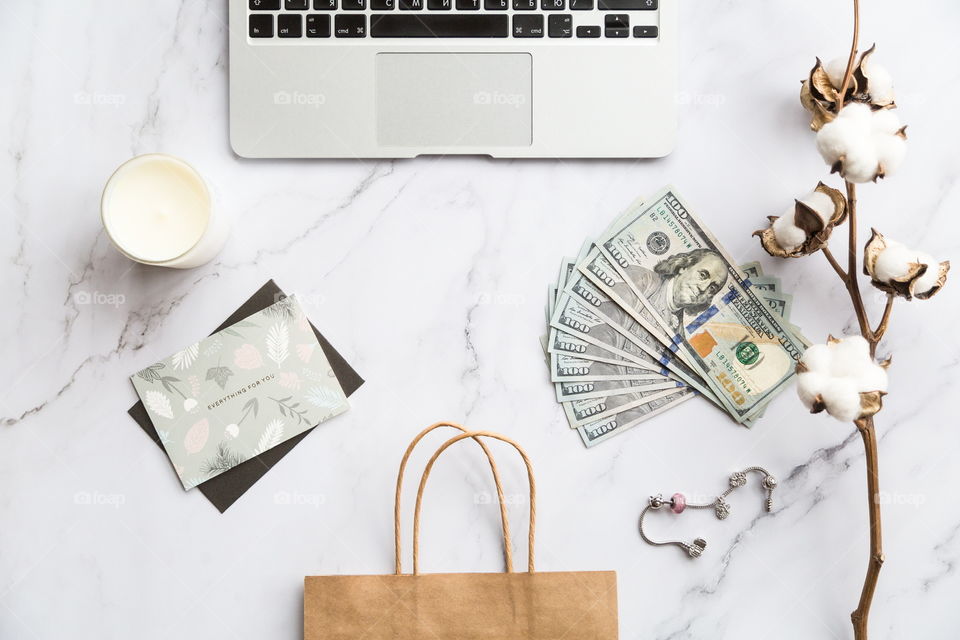 Holiday shopping. Flatlay items. Laptop, cash money, one hundred dollars bill, bag, cotton flowers, card, candle. Online 